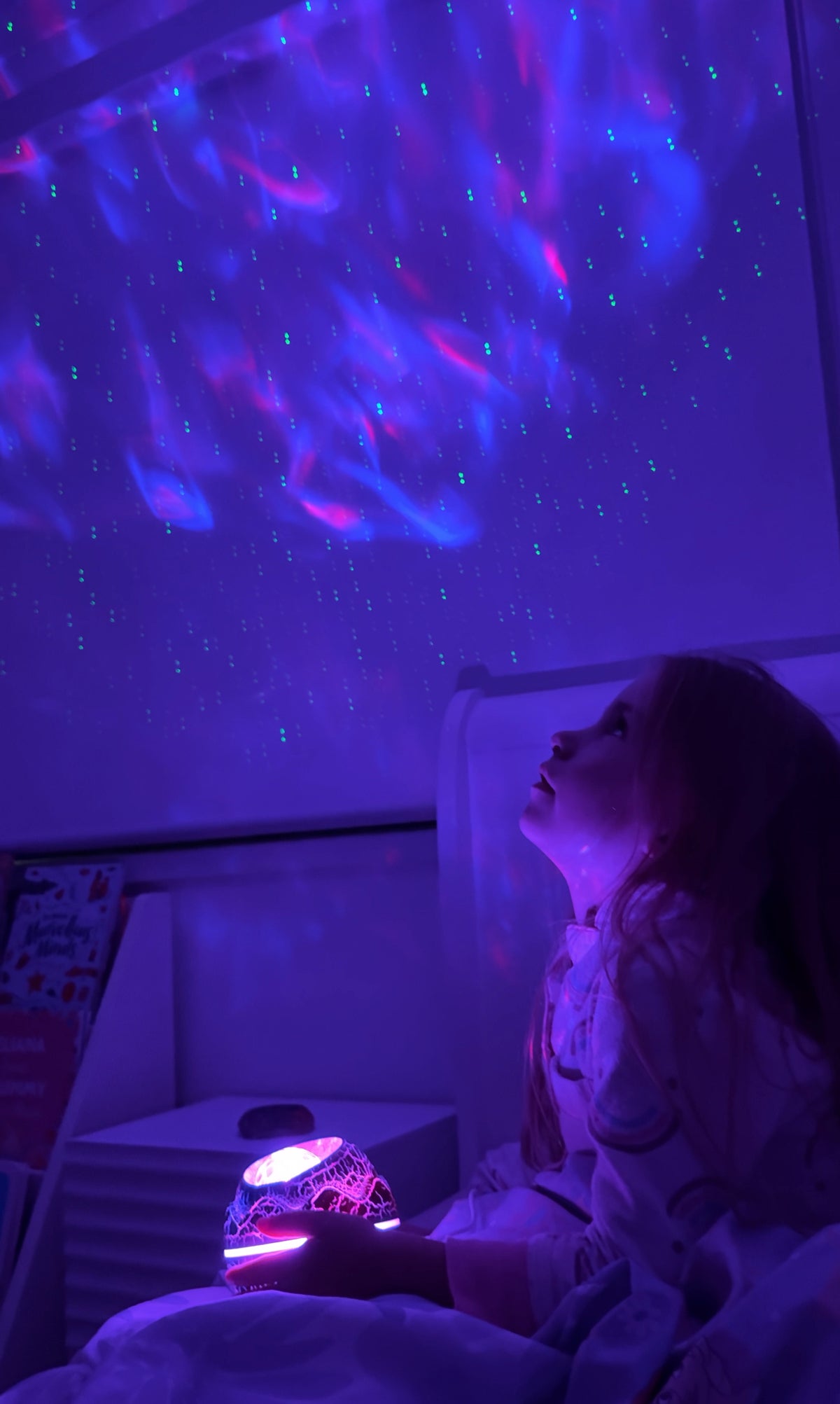 Child gazing at the purple colours on the ceiling of their bedroom enjoying their nightlight